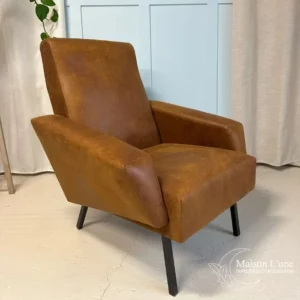 fauteuil couleur cognac pieds métal noir visible de face sur fond bleu glacier avec moulures et rideaux gris clair