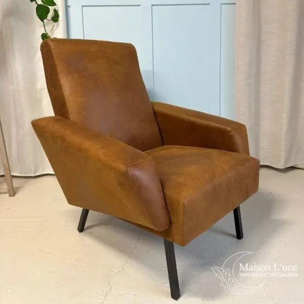 fauteuil couleur cognac pieds métal noir visible de face sur fond bleu glacier avec moulures et rideaux gris clair