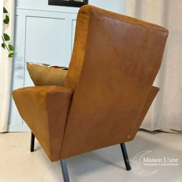 fauteuil couleur cognac pieds métal noir visible de dos sur fond bleu glacier avec moulures et rideaux gris clair