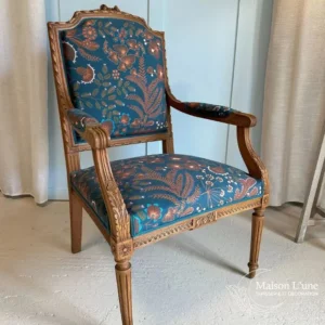 Fauteuil style Louis XVI au motif végétal marron sur fond bleu pétrole. Le bois du fauteuil est sculpté d'ornements