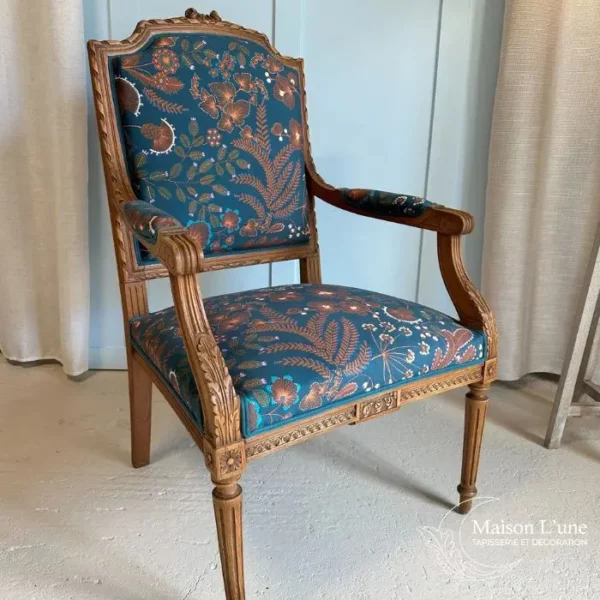 Fauteuil style Louis XVI au motif végétal marron sur fond bleu pétrole. Le bois du fauteuil est sculpté d'ornements